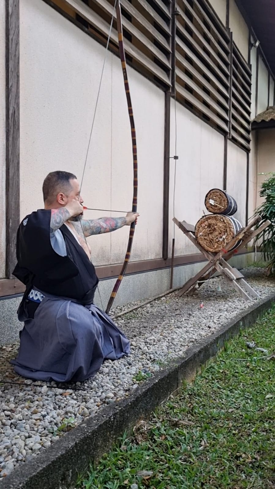 Praticante ajoelhado com arco diante de alvos de palha