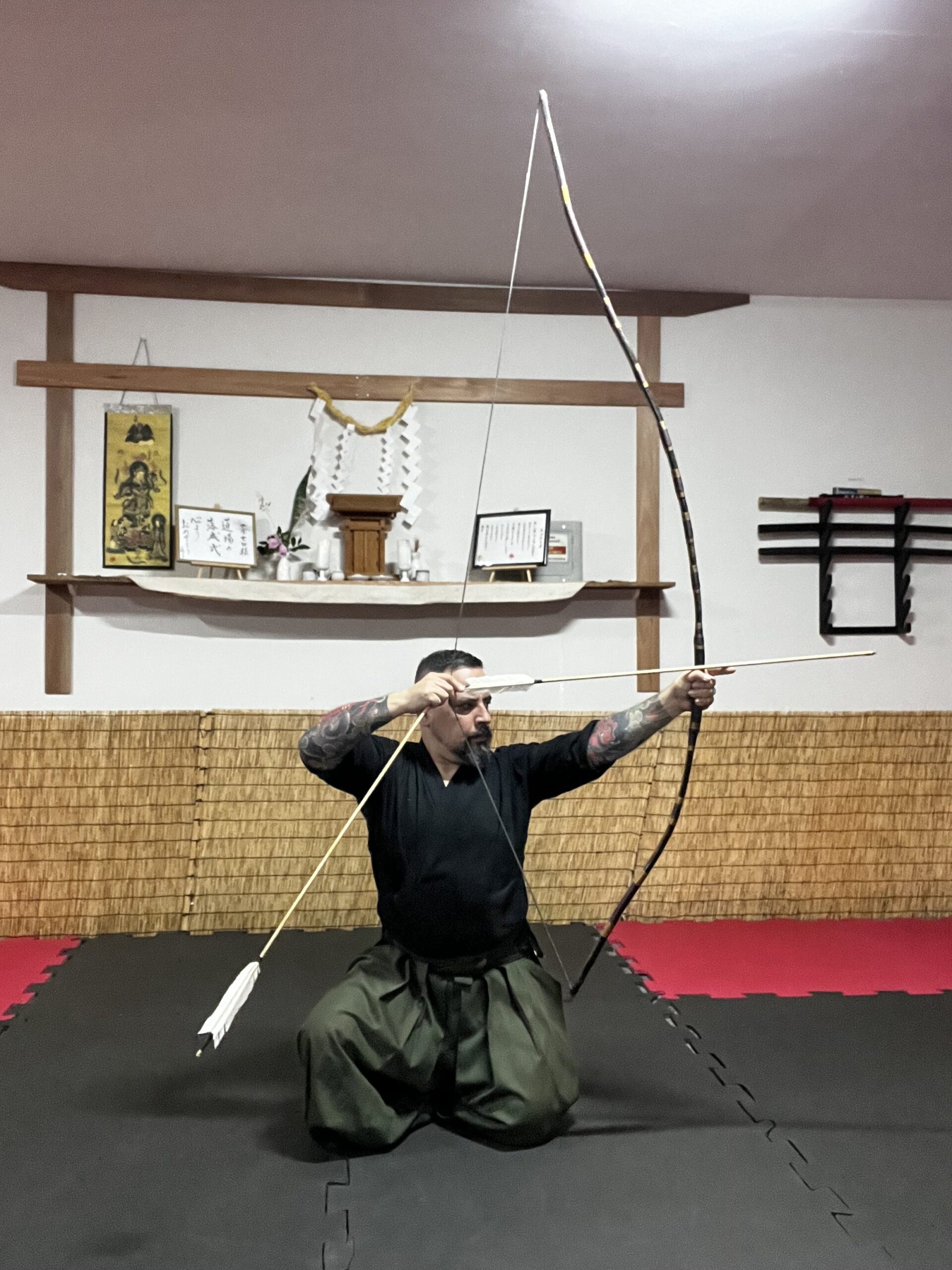 Jason Sensei pratica com o arco em postura ajoelhada no dōjō